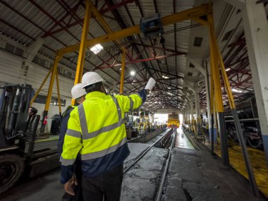 Üniformalı ve kasklı bir erkek işçi fabrikada vinç kullanıyor. Endüstriyel üretim, metal mühendisliği, güç makineleri üretimi