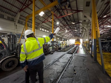 Üniformalı ve kasklı bir erkek işçi fabrikada vinç kullanıyor. Endüstriyel üretim, metal mühendisliği, güç makineleri üretimi