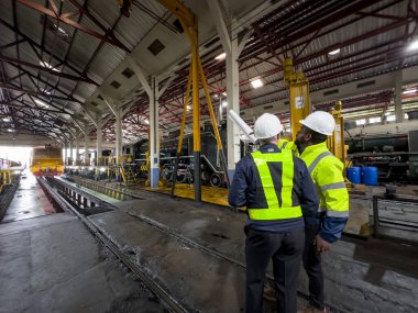 Üniformalı ve kasklı bir erkek işçi fabrikada vinç kullanıyor. Endüstriyel üretim, metal mühendisliği, güç makineleri üretimi