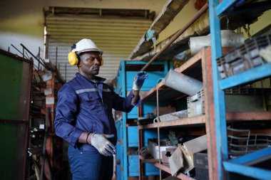 Young successful technician or repairman of industrial machines in safety helmet and workwear standing in large garage or workshop