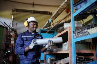 Young successful technician or repairman of industrial machines in safety helmet and workwear standing in large garage or workshop
