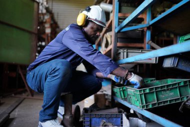 Young successful technician or repairman of industrial machines in safety helmet and workwear standing in large garage or workshop