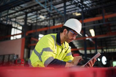 Young successful technician or repairman of industrial machines in safety helmet and workwear standing in large garage or workshop