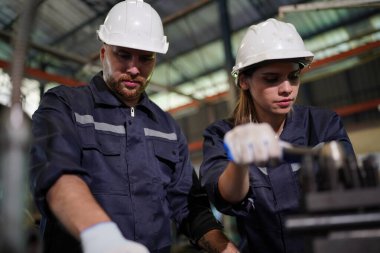 Young successful technician or repairman of industrial machines in safety helmet and workwear standing in large garage or workshop