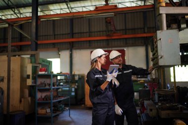 Young successful technician or repairman of industrial machines in safety helmet and workwear standing in large garage or workshop