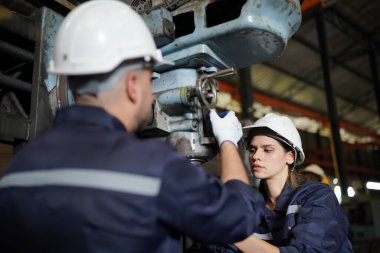 Young successful technician or repairman of industrial machines in safety helmet and workwear standing in large garage or workshop