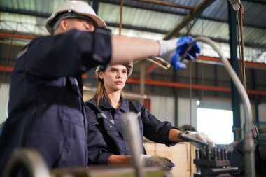 Young successful technician or repairman of industrial machines in safety helmet and workwear standing in large garage or workshop