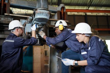 Young successful technician or repairman of industrial machines in safety helmet and workwear standing in large garage or workshop