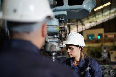 Young successful technician or repairman of industrial machines in safety helmet and workwear standing in large garage or workshop