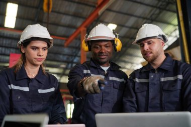 Young successful technician or repairman of industrial machines in safety helmet and workwear standing in large garage or workshop