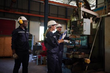 Young successful technician or repairman of industrial machines in safety helmet and workwear standing in large garage or workshop