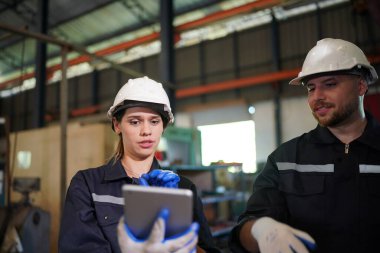 Young successful technician or repairman of industrial machines in safety helmet and workwear standing in large garage or workshop