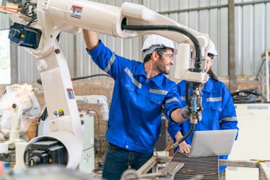 Robot mühendisleri fabrika deposunda modern robotik kolun bakımı üzerinde çalışıyorlar.