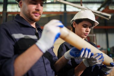 Young successful technician or repairman of industrial machines in safety helmet and workwear standing in large garage or workshop