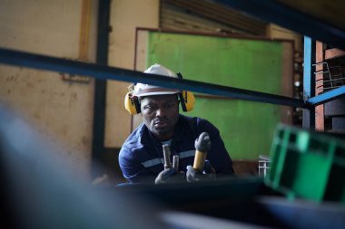 Young successful technician or repairman of industrial machines in safety helmet and workwear standing in large garage or workshop