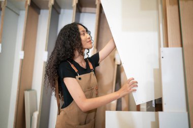 Mobilya atölyesi modern tasarımda geleneksel becerileri kullanarak çağdaş mobilya parçaları üretiyor. Kulak koruyucuları elinde odun tutan, makine kullanan bir adam..