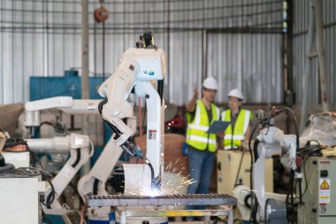 Robot mühendisleri fabrika deposunda modern robotik kolun bakımı üzerinde çalışıyorlar.