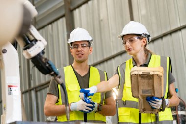 Robot mühendisleri fabrika deposunda modern robotik kolun bakımı üzerinde çalışıyorlar.