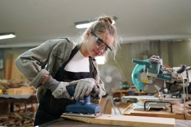 Marangoz DIY atölyesinde çalışan genç ve güzel bir kadın. Küçük işletme sahibi, mobilya fabrikasında çalışan genç bir kadın..