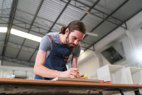 A furniture workshop making bespoke contemporary furniture pieces using traditional skills in modern design. A man in ear defenders holding wood, using a machine.