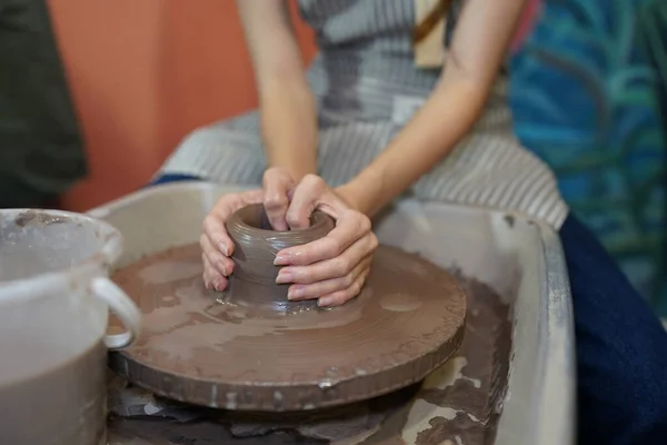 Close-up of concentrated craftswoman in apron sitting at pottery wheel