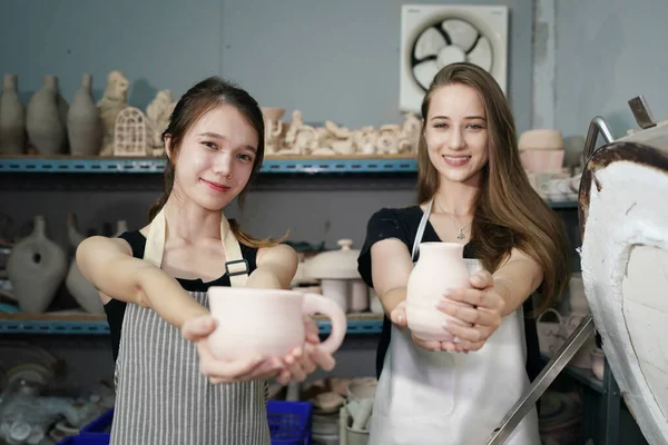 Beautiful young woman ceramic artist holding clay bowl and smiling while standing in pottery workshop