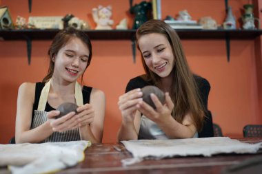 Zanaatkar kadınlar masada oturuyor ve kilden vazolar ve çömlekçilikle çalışıyor, iş sahibi.