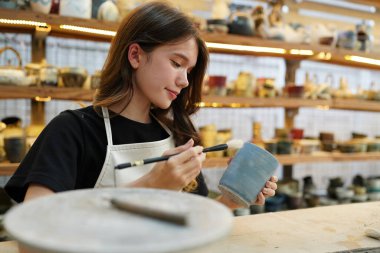 Çömlekçide oturan önlüklü güzel zanaatkar kadının yakın çekimi.