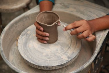 Konsantre olmuş, önlüklü, çömlek direksiyonunda oturan ve ıslak kil kabı şekillendirirken el işi aletleri kullanan güzel bir zanaatkar.