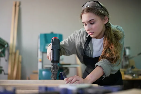 stock image Small business of a young woman. Beautiful young woman worker in a furniture workroom, measuring wood.