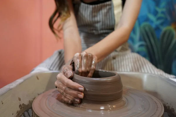 制作湿黏土器皿时 穿着围裙坐在陶瓷轮旁 使用手工工具的女工匠近景 — 图库照片