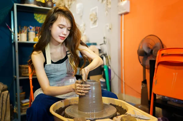 聚精会神漂亮的围裙女工匠坐在陶瓷轮旁 用手工工具塑造湿黏土器皿的特写 — 图库照片