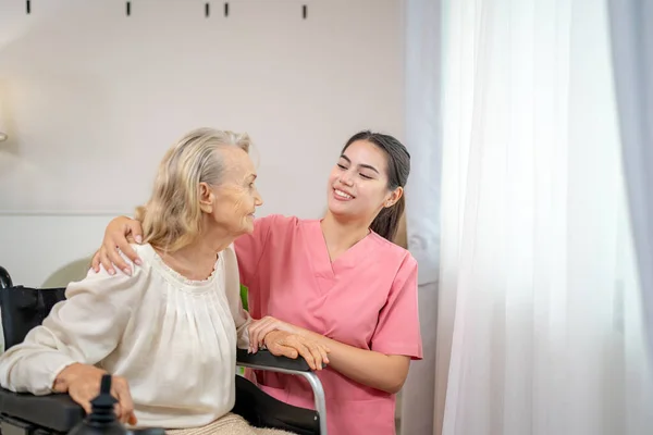 Elderly woman and nurse at home. Healthcare worker girl cares about senior female person indoors