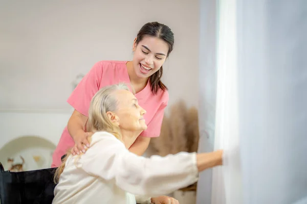 Elderly woman and nurse at home. Healthcare worker girl cares about senior female person indoors