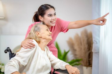 Evde yaşlı bir kadın ve hemşire var. Sağlık hizmetleri çalışanı kız, evin içindeki yaşlı bayanı önemser.