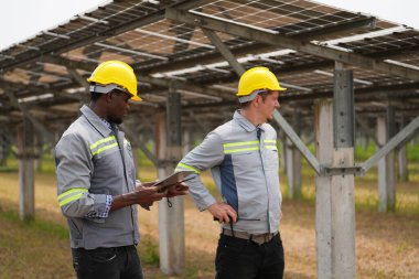 Fotovoltaik bir çiftlikte çalışan elektrik mühendisleri, güneş enerjisi endüstrisindeki aletlerle kontrol ve bakım ekipmanlarını kontrol ediyorlar..