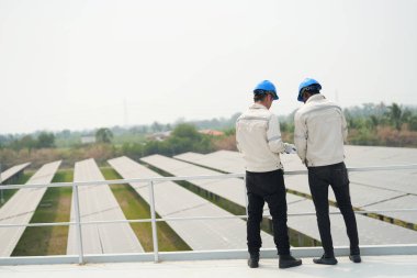 Fotovoltaik bir çiftlikte çalışan elektrik mühendisleri, güneş enerjisi endüstrisindeki aletlerle kontrol ve bakım ekipmanlarını kontrol ediyorlar..