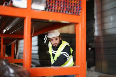 Depoda çelik yelek giyen erkek işçi yazıyor.