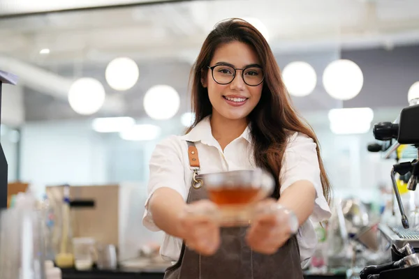 Portrait of happy woman standing in her store. Cheerful waitress waiting for clients at coffee shop. Successful small business owner in casual wearing grey apron
