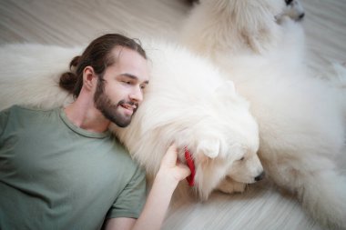 Köpekleriyle evde eğlenen genç bir adam. 