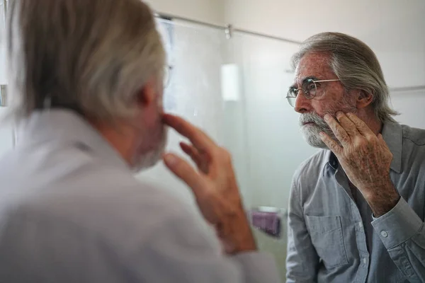 old man with gray hair checking hair in front of mirror