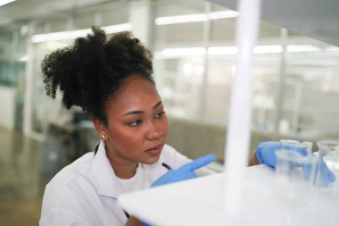 Laboratuvardaki bilim adamı, laboratuarda yaptığı deneyler sırasında numune alıp incelerken arka planda meslektaşları da vardı.