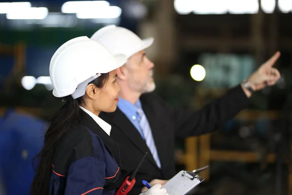 Factory manager and female engineer in factory and inspecting factory in industry plant background.