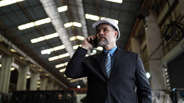 Factory manager or businessman owner in factory warehouse is talking on mobilephone. Business industry background.