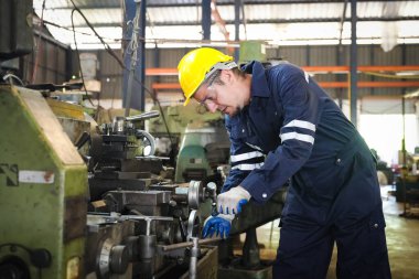 Torna operatörü işine odaklandı. Üniformalı ve kasklı işçiler torna tezgahında çalışıyor, fabrikada. Endüstriyel üretim, metal mühendisliği, imalat.