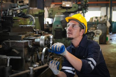 Torna operatörü işine odaklandı. Üniformalı ve kasklı işçiler torna tezgahında çalışıyor, fabrikada. Endüstriyel üretim, metal mühendisliği, imalat.