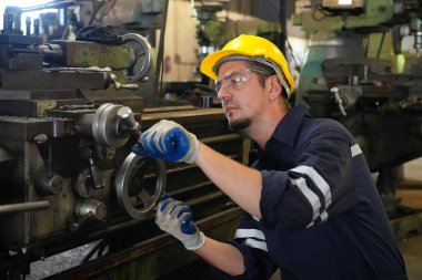 Torna operatörü işine odaklandı. Üniformalı ve kasklı işçiler torna tezgahında çalışıyor, fabrikada. Endüstriyel üretim, metal mühendisliği, imalat.