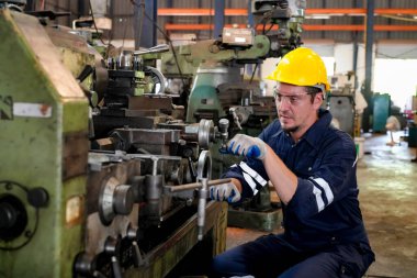 Torna operatörü işine odaklandı. Üniformalı ve kasklı işçiler torna tezgahında çalışıyor, fabrikada. Endüstriyel üretim, metal mühendisliği, imalat.