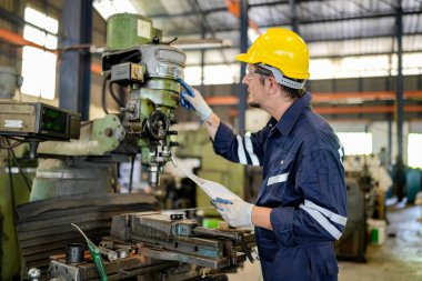 Torna operatörü işine odaklandı. Üniformalı ve kasklı işçiler torna tezgahında çalışıyor, fabrikada. Endüstriyel üretim, metal mühendisliği, imalat.