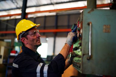 Torna operatörü işine odaklandı. Üniformalı ve kasklı işçiler torna tezgahında çalışıyor, fabrikada. Endüstriyel üretim, metal mühendisliği, imalat.